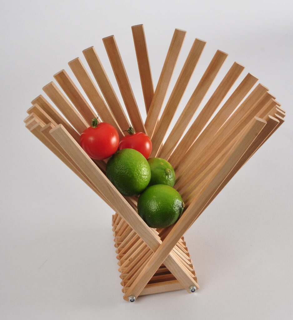 Eine wandelbare Schale aus vielen Holzstreifen, in ihr liegen Tomaten und Limetten.