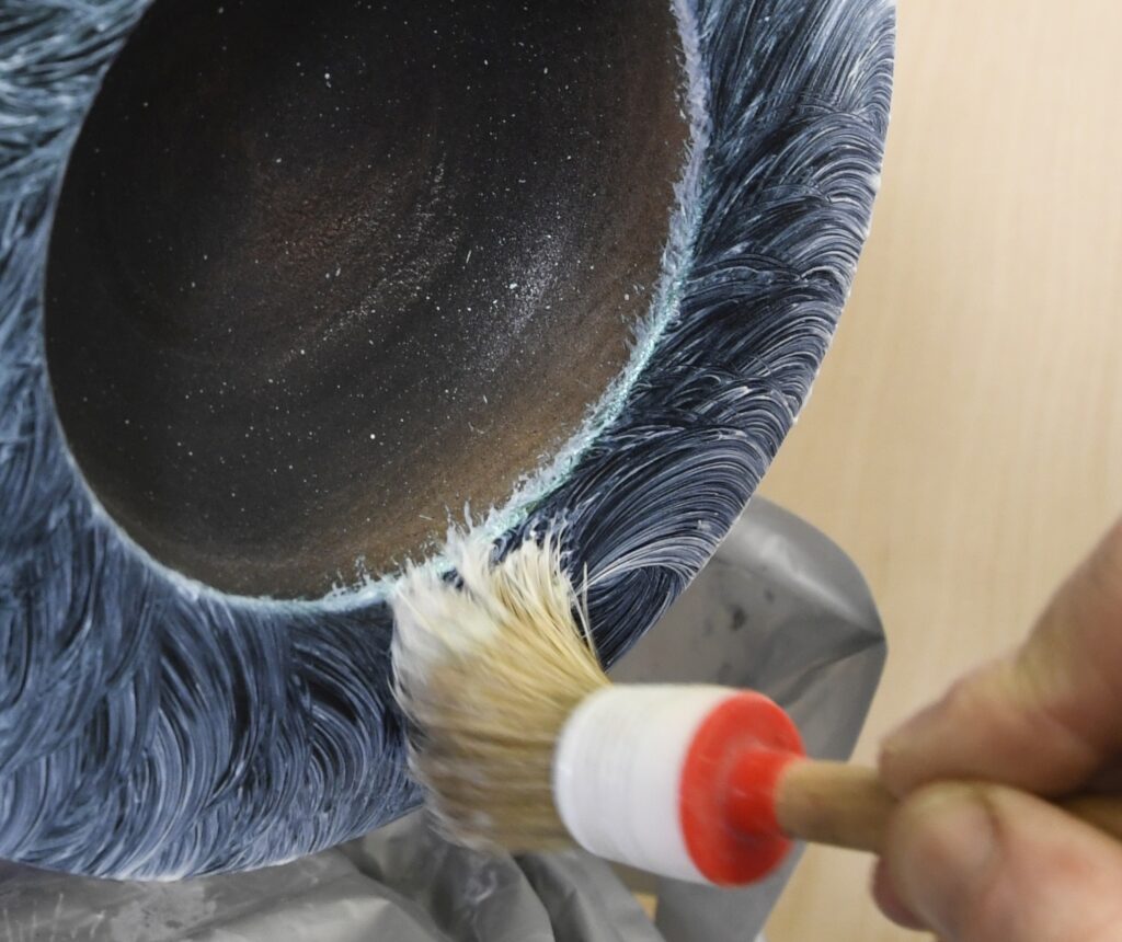 Eine Drechselschale wird mit Effektfarbe und einem Pinsel bearbeitet.