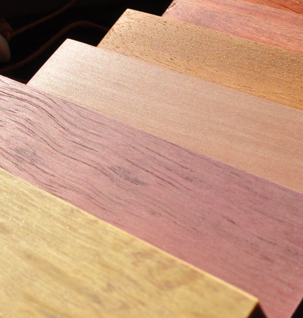 Werkstoff Holz: So unterschiedlich kann Holz sein. Das zeigen die aufeinandergelegten kleinen Holzproben von Hölzern unterschielichster Färbung in gelb, rosa, Brauntönen.