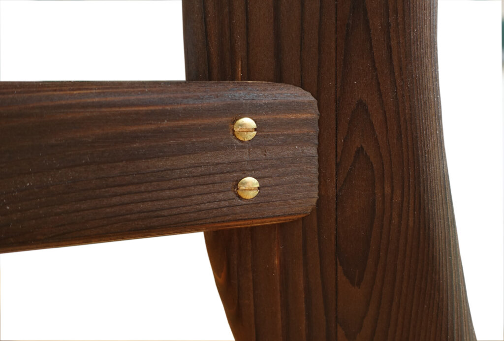 Detailfoto von der Zargenverbindung des Tisches. Zwei Messingschrauben zieren die Verbindung auf dem schokobraunen Holz.