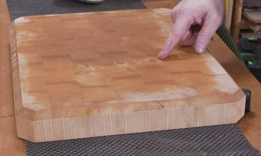 Ein Fleck ist auf dem fertig aufgearbeiteten Brett noch zu sehen. Ein Finger deutet auf ihn.