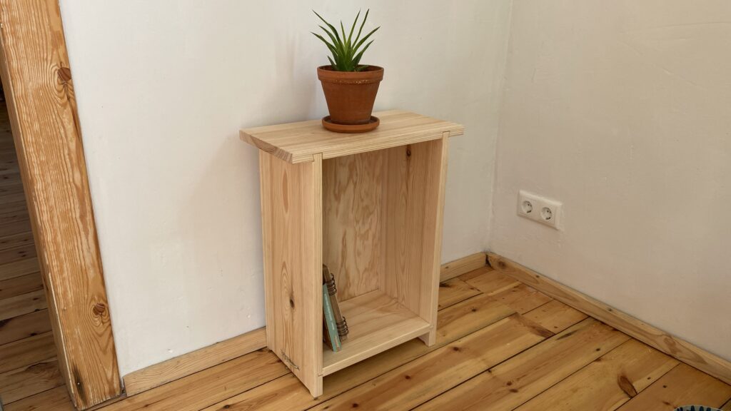 Das fertige Schränkchen mit Blumentopf als Dekoration steht in einer Zimmerecke,