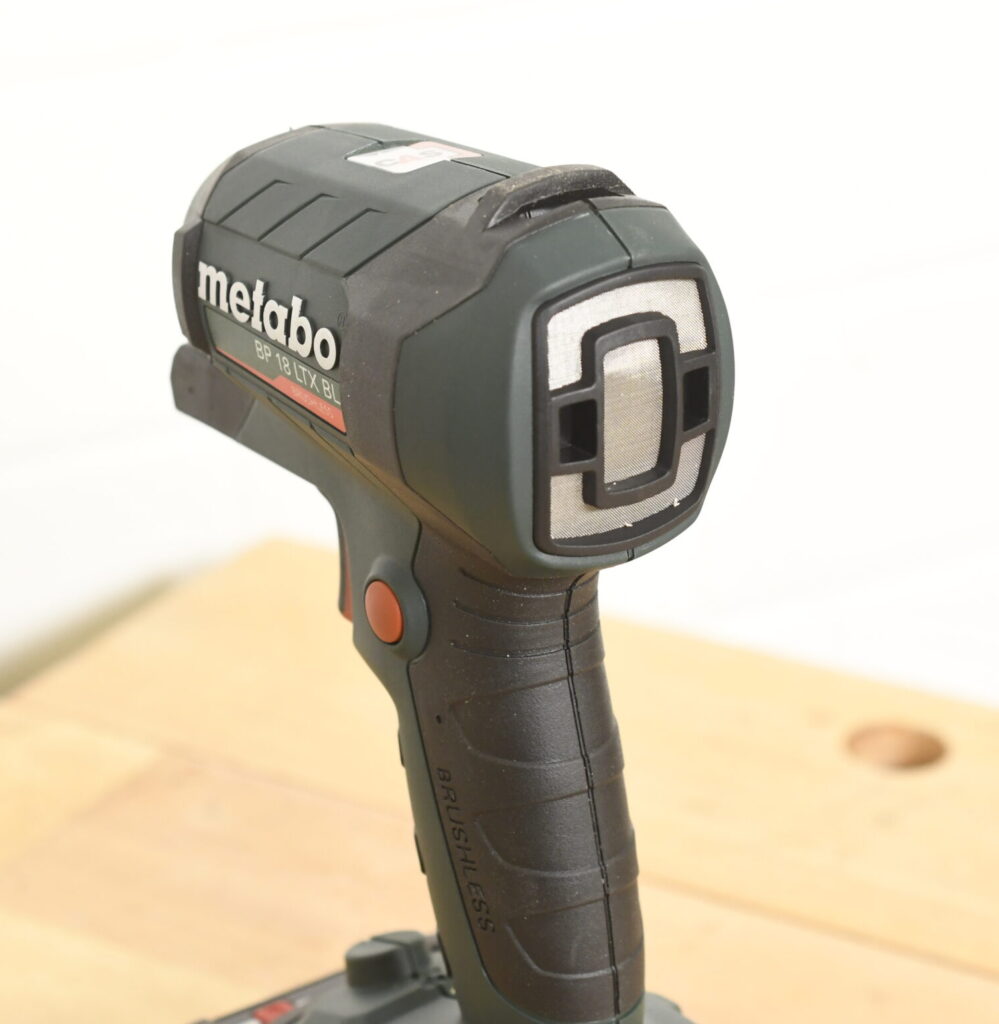 Nahaufnahme einer kabellosen Metabo-Blaspistole, Modell „BP 18 LTX BL“. Die Blaspistole ist schwarz-grün mit roten Akzenten, hat einen ergonomischen Griff und eine markante Ausblasöffnung an der Vorderseite.