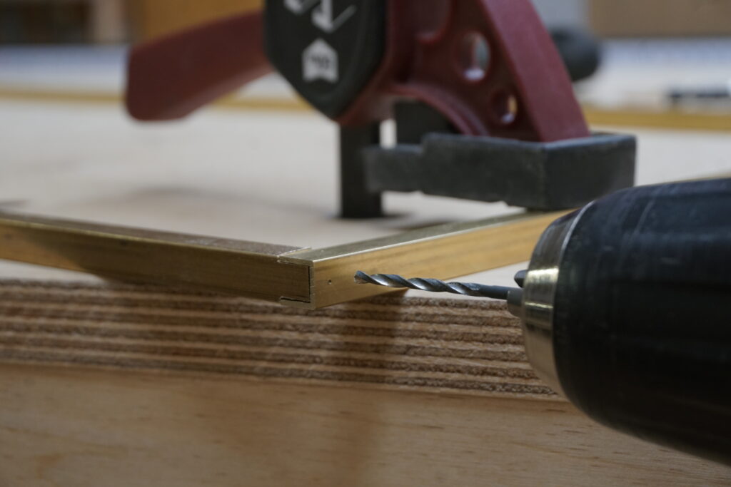 Titelthema HolzWerken 120 ist das Lowboard in Eiche. Das Detailbild zeigt einen Metallbohrer, der ein Loch in ein U-Profil aus Messing bohrt.