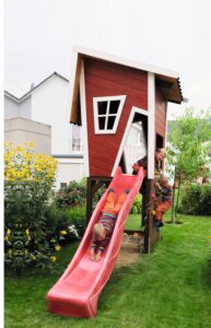Rotes Spielhaus aus Holz mit einer Rutsche, auf der ein Kind gerade rutscht.