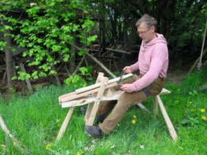 Ein Mann sitzt an einem Hobelpferd im Garten.