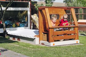 Sandkasten in Form eines LKWs. Im Fahrerhaus sitzen zwei Kinder.