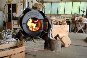 Ein Ofen steht in einer Werkstatt. Im Ofen brennt ein Feuer.