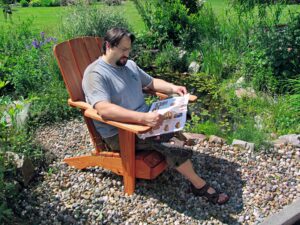 Ein Mann sitzt in einem Gartenstuhl auf der Terrasse und liest in einer Zeitschrift.