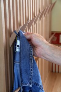 Eine Hand hängt eine Jacke am Haken einer selbstgebauten Garderobe aus Holz auf.