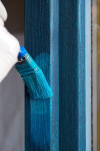 Mit einem Pinsel wird ein Fensterrahmen blau lasiert.