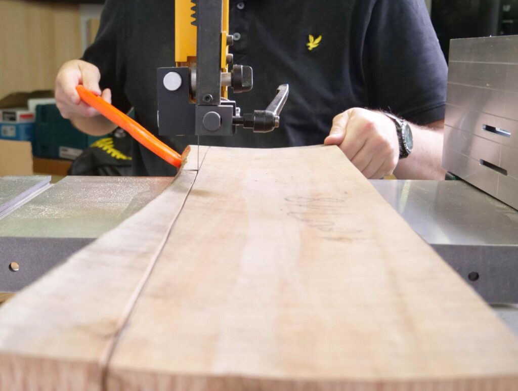 Ein sägeraus Brett wird an der Bandsäge nach Riss besäumt.