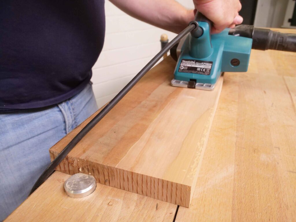 Ein Mann hobelt eine raue Fläche mit einem elektrischen Handhobel