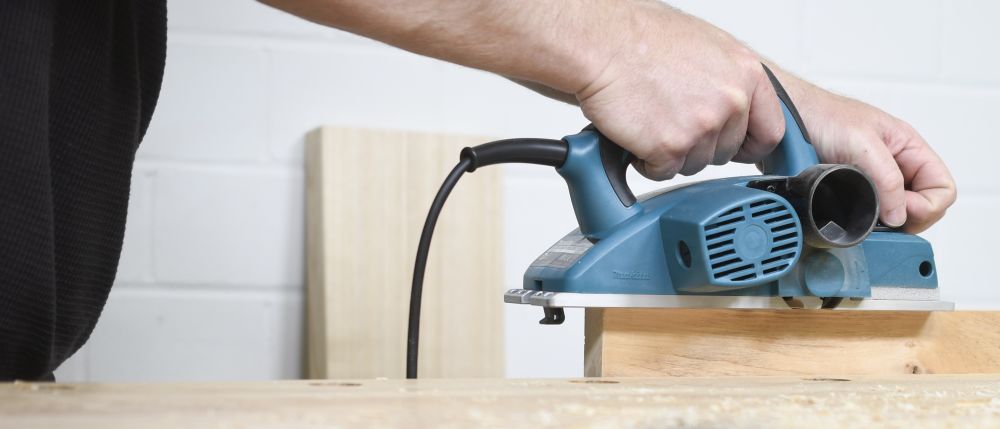 In der HollzWerken-Ausgabe 122 geht es um Elektrohobel. Im Bild schieben zwei Hände einen blauen Elektrohobel über ein eingespanntes Werkstück aus Holz.