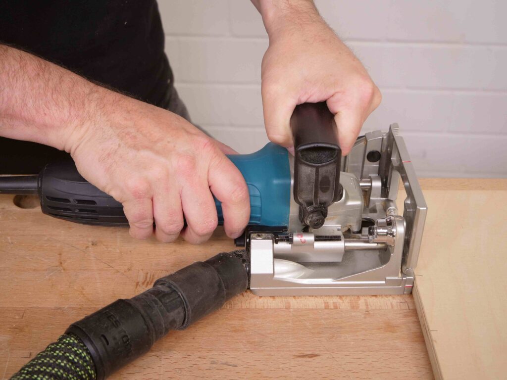 Ein Mann drückt eine Flachdübelfräse an die Kante einer Holzplatte