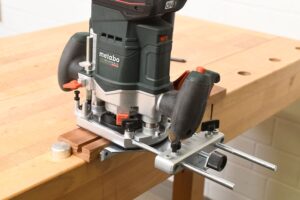 Die Oberfräse OFV 18 LTX-BL 12 von Metabo sitzt mit Parallelanschlag auf einem Brett