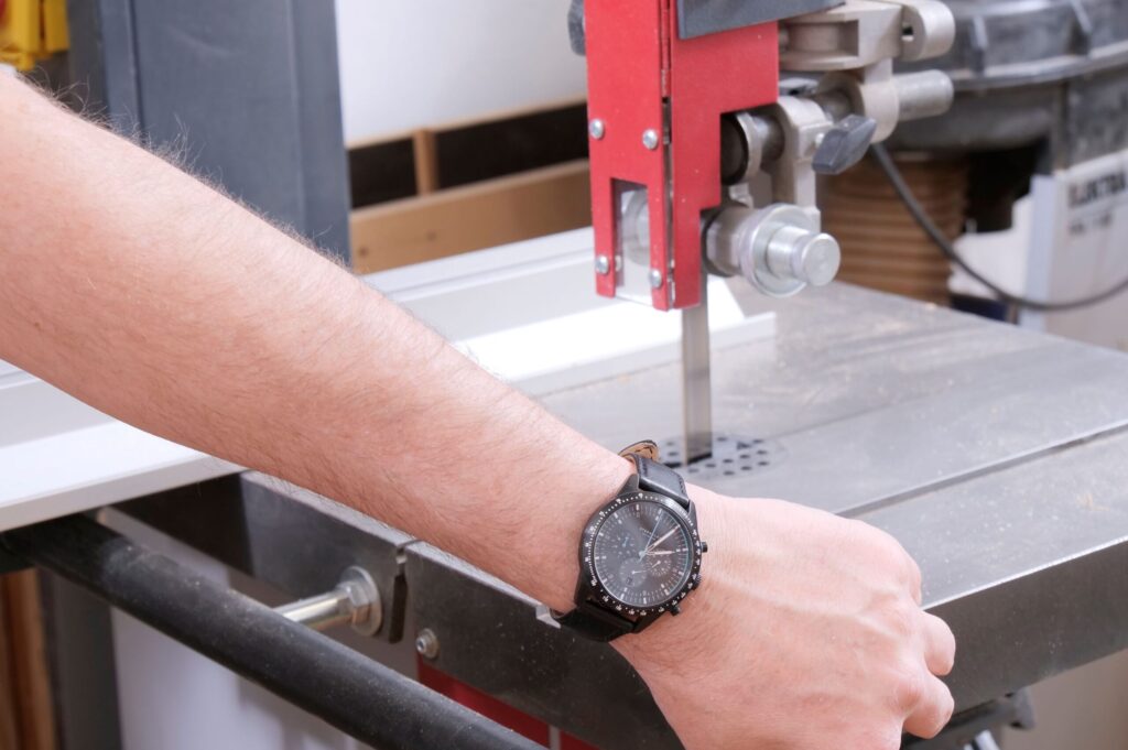 Ein Arm mit Armbanduhr wird vor eine Bandsäge gehalten