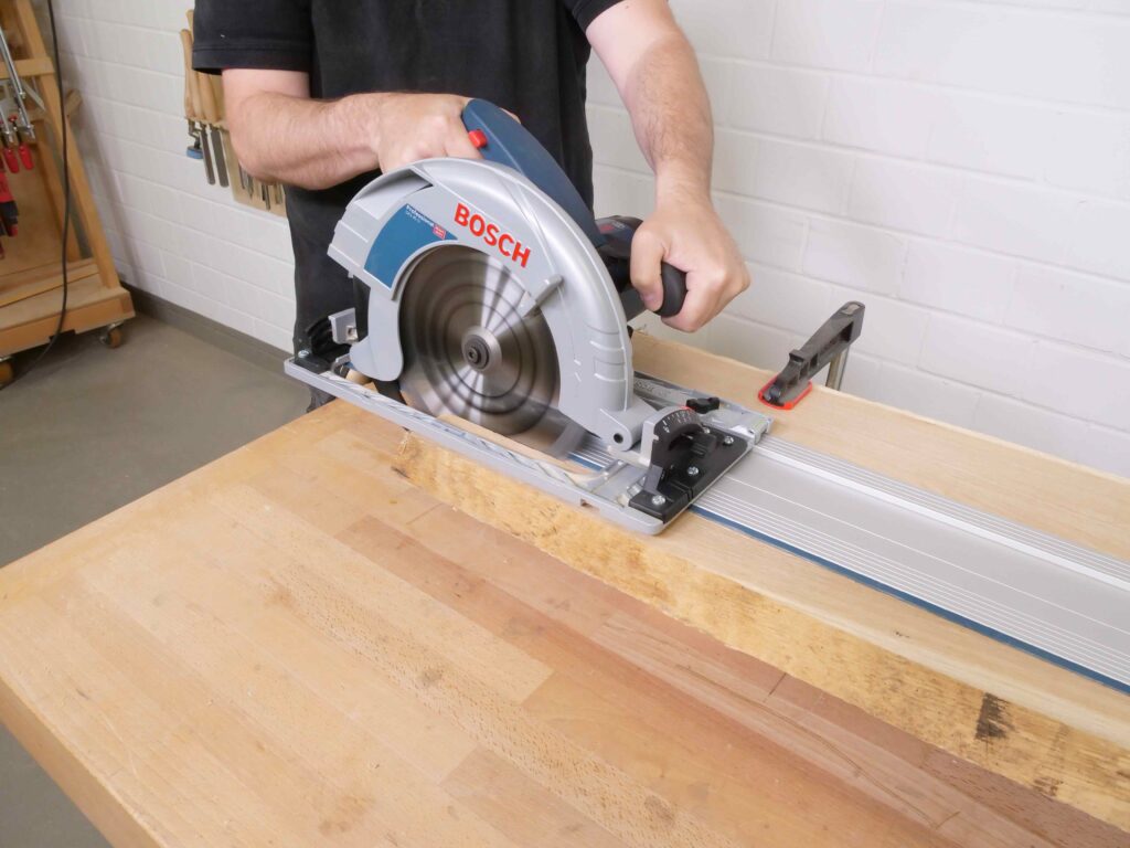 Ein Mann sägt eine Bohle längs mit einer Handkreissäge durch