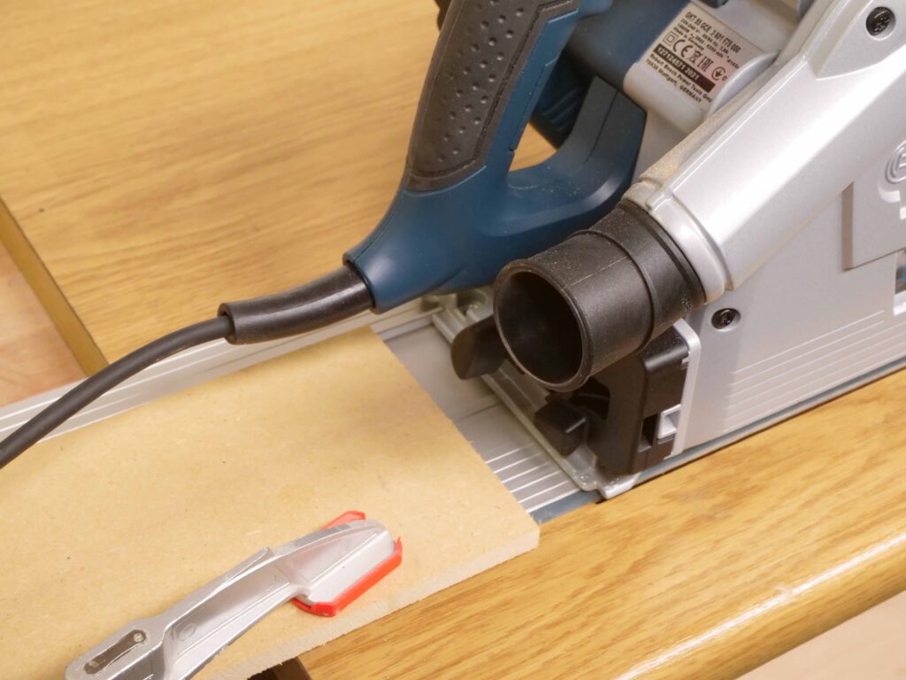Eine einfache MDF-Platte ist als Rückschlagschutz hinter einer Handkreisssäge auf einer Schiene befestigt