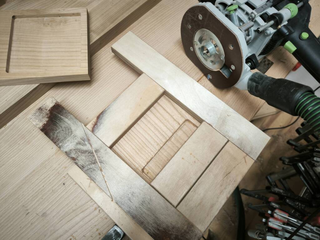 Das Werkstück liegt in der Vorrichtung zum Fräsen des Tablars, daneben eine Oberfräse.