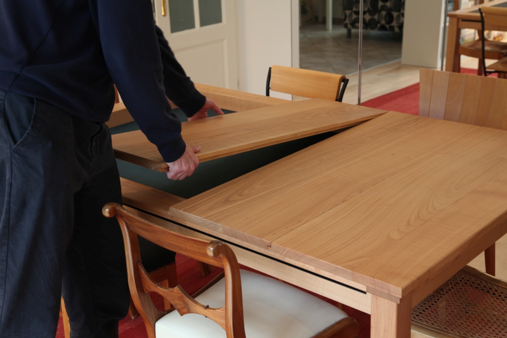 Eine Person hält ein Teilelement der Plattenabdeckung des Tisches in den Händen. Darunter ist der Blick auf den Spieltisch frei.