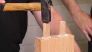 Ein Mann schlägt mit einem Hammer Holzdübel ein