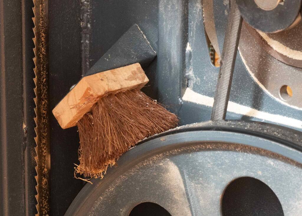 Kleine Bürste aus Holz und Naturborsten reinigt das Antriebsrad einer Bandsäge von Sägemehl.