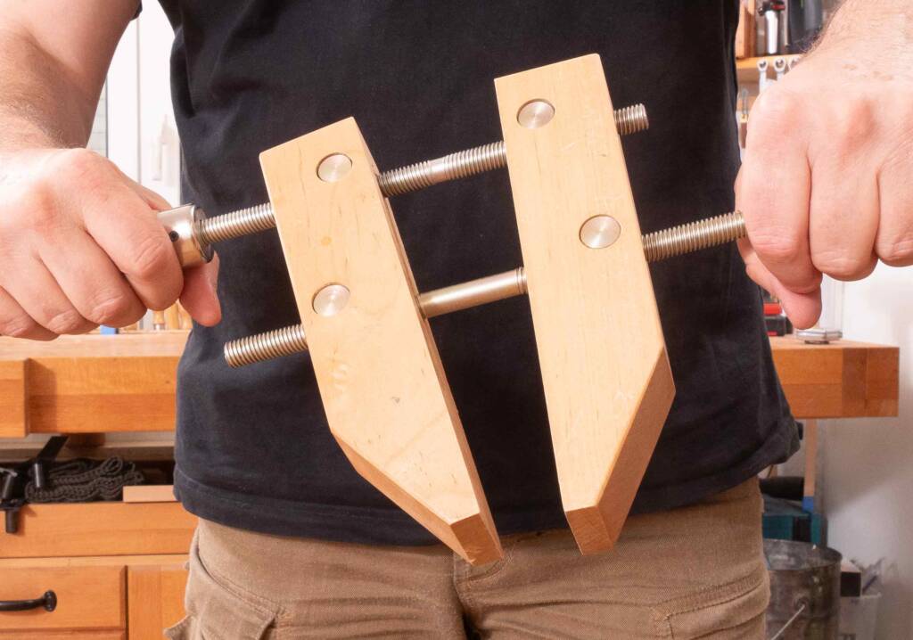 Person hält eine Parallelzwinge aus Holz mit zwei Gewindespindeln in einer Werkstatt fest.