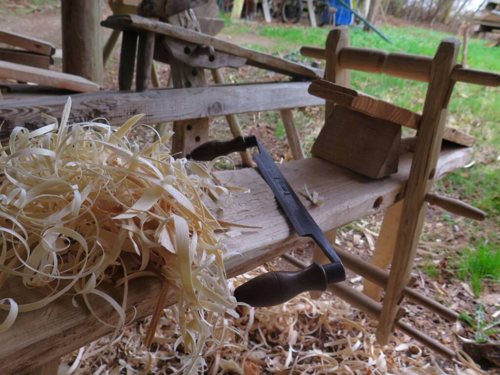 Holzbank mit Spänen, Zugmesser und Hobel in einer rustikalen Außenwerkstatt.