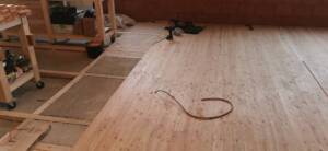 Der halbfertige Holzfußboden in der Werkstatt von Holzwerker Gerhard Nagy. Auf de Fläche ragt ein Kabel heraus, am linken Bildrand stehen auf dem noch nicht belegten Estrich Werkstattwagen aus Holz mit Geräten und Material darauf.